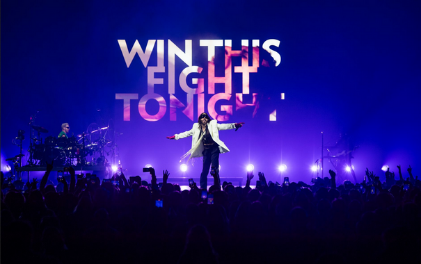 Blue scenario with big text in white and pink: Win This Fight Tonight.
Jared Leto is wearing a white jacket on the stage and the crowd in dark blue is raising thier arms.


Photography by Andrew Timms
