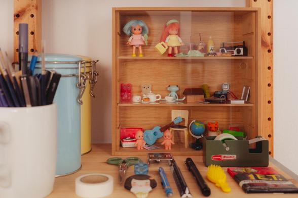 Picture of a shelf in my studio with a tiny cabinet containing even tinier and colorful toys. Next to it there are some art supplies, also colorful and nicely arranged.