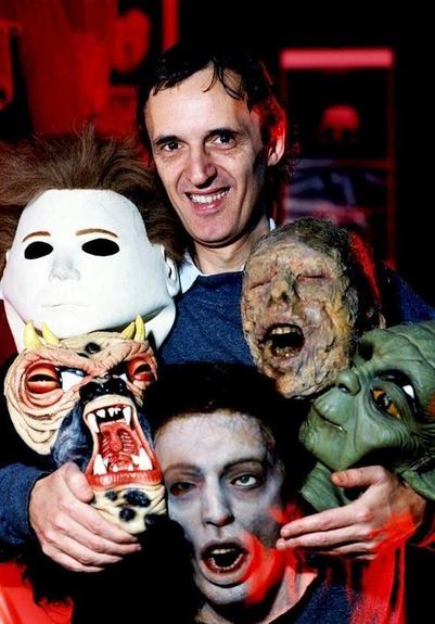 Dario Argento with a collection of iconic horror masks and props. https://i.pinimg.com/564x/7e/01/3a/7e013a7d78fc40cdb0187ba204adff69.jpg