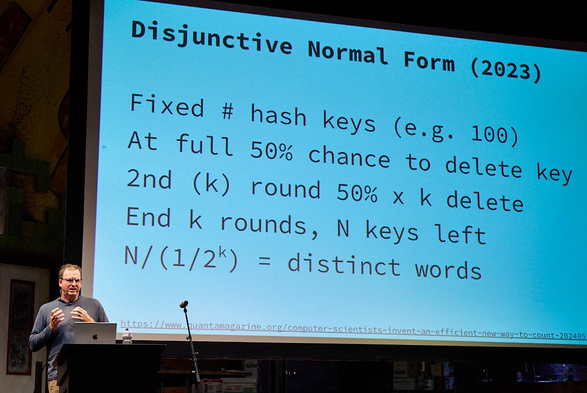 Speaker behind a lectern with screen showing a breakdown of the disjunctive normal form algorithm 