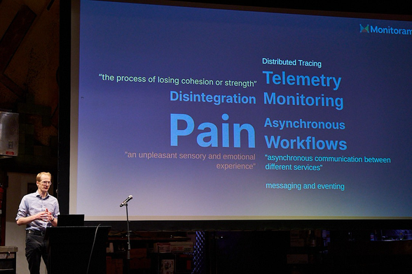 Speaker on stage in front of slide explaining the definition of words in the title: pain: An unpleasant sensory and emotional experience disintegration: the process of losing cohesion or strength workflows: asynchronous communication between different services messaging and eventing