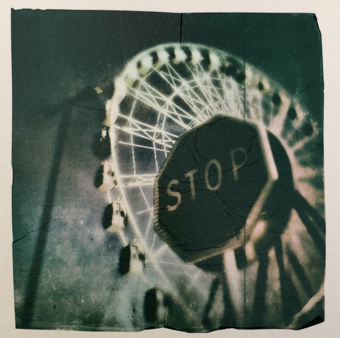 A ferris wheel with a stop road sign in front of it. Polaroid emulsion lift.
