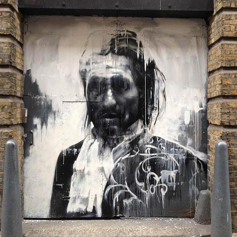 a painting on the wall of a building, bricks bookending it, it is of a figure wearing gentleman's jacket and ruffled poet's shirt, done in black and white, lots of drip and splatter effects, he looks weary, he is looking to the right of the viewer, some floral designs scrawled on his chest on the right side