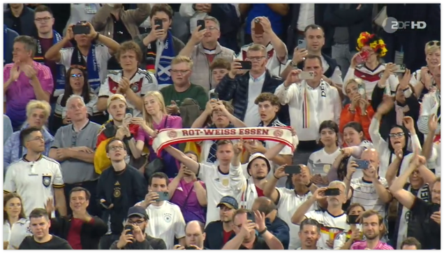 Fußballfans auf der Tribüne. Ein Mann hält einen Schal von Rot-Weiss-Essen hoch.