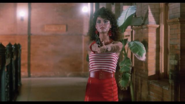A woman in a red and white striped top and red skirt is aiming a gun in a scene with brick walls and plants in the background.