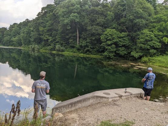 Photo of my partner and our friend fishing at a large pond at our local state park with trees in the background.