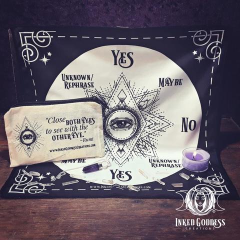 The contents of our Third Eye Pendulum Kit are arrayed on a dark wooden surface. A square black altar cloth is partially strung up as a backdrop. It has a large beige circle in the center with third eye imagery line art. Arranged onat 8 points around the circle are the words "Yes," "No," "Maybe," and "Unknown/Rephrase." Each word is on the cloth twice, at opposite points on the circle. A brown canvas zipper bag is propped on the hung cloth and has a version of the same third eye line art with the text, "Close both eyes to see with the other eye," attributed to Rumi. An amethyst point gemstone pendulum is shown as well as a purple tealight for scale. This is an exclusive product from Inked Goddess Creations.