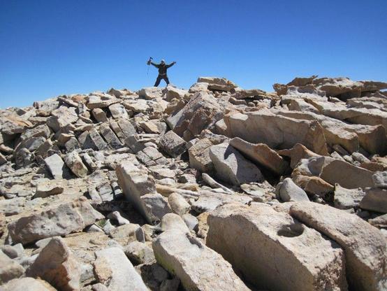 Hack the peak-end rule to maximize conference impact: photograph of a person, silhouetted against the sky, making a triumphant gesture at the top of a rocky hill