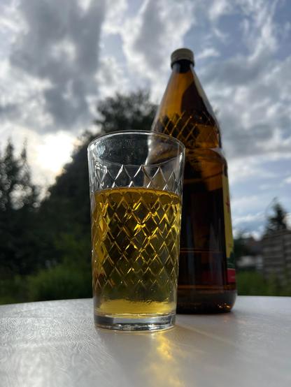 Ein Rippeglas mit Apfelweinflasche vor einem Garten-Hintergrund 