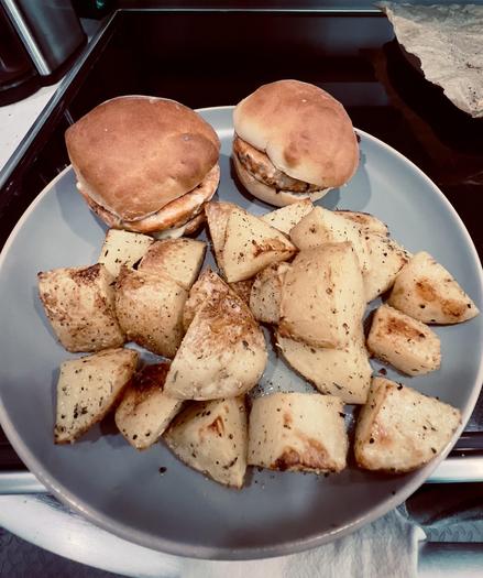 Two sandwiches with browned buns and a generous portion of roasted potato wedges on a gray plate.