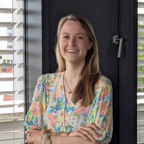 Fotografisches Portrait der NaWik Mitarbeiterin Helen Zimmermann im Besprechungsraum des NaWik vor einer Fensterwand. 