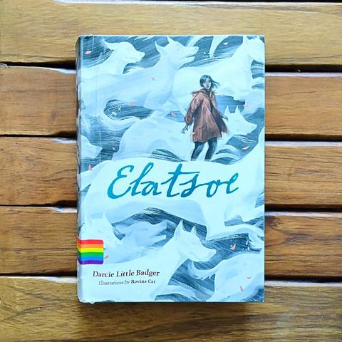 Photo of Darcie Little Badger's book Elatsoe. On the cover there is a young Native American girl, who is surrounded by a pack of running white ghost dogs.