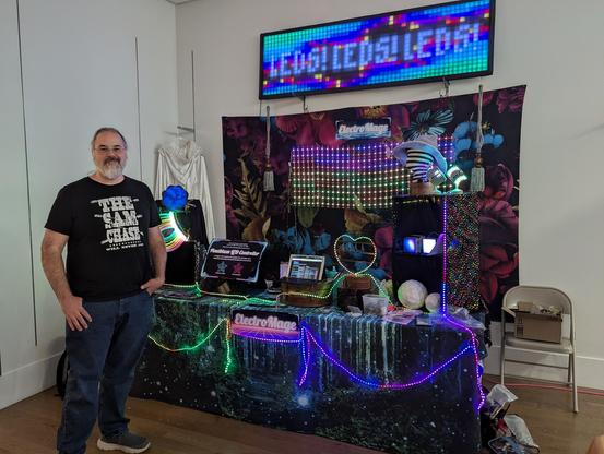 Ben Hencke standing in front of a display booth showcasing LED art run by the Pixelblaze controller 