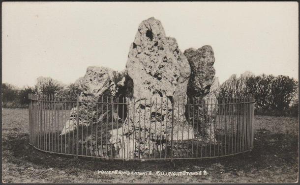 A vintage black and white photographic postcard showing the dolmen or chambered tomb called the Whispering Knights, which stands on the opposite side of the same field as the Rollright Stones in Oxfordshire, and close to the border with Warwickshire. An isolated menhir, the King Stone, stands across the county border on the other side of the road. The stones of all three monuments are oolitic limestone.