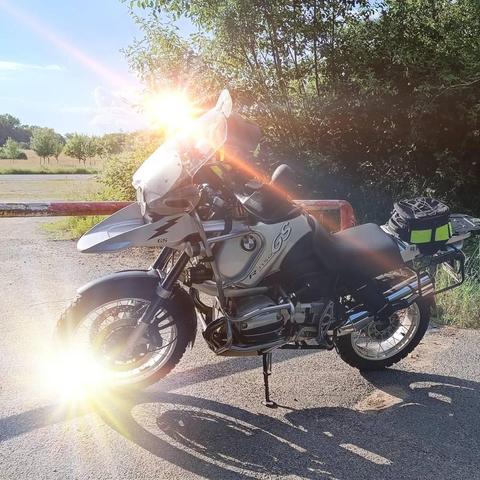 BMW R1150GS steht an einer Schranke und die Abendsonne spiegelt sich in der Vorderradfelge.