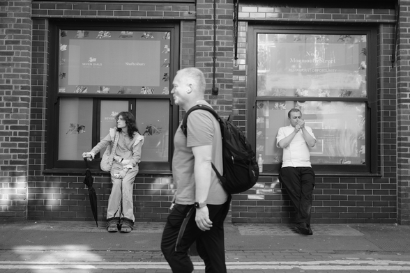 Two people sit on windowsills as another person walks in front of them.