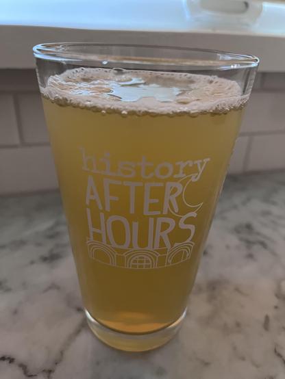 Photograph of a pint glass (that reads “History After Hours” and has a picture of the Washington State History Museum). The glass contains a lightly cursed shandy made of Vitamin Water Zero and a nonalcoholic beer. 
