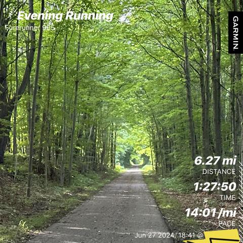 A paved path through a forest during an evening run with statistics overlaid: 6.27 miles distance (10.09 km), 1:27:50 time, and 14:01 minutes per mile pace (8:42 per km). Date: June 27, 2024,