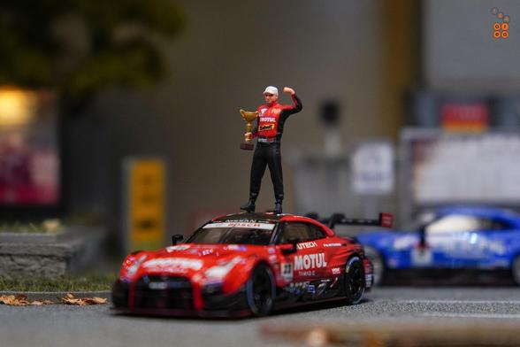 A driver with a thophy celebrating on car roof of Nissan GT-R Nismo GT500 No.23 “MOTUL AUTECH GT-R" NISMO ​2021 SUPER GT SERIES by MINI GT in 1:64 scale with 1:64 figure on AREA 164