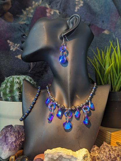Handmade set called Siren Call Set including a necklace with hematite styled beads and purple beads and lots of faceted glass purple shell, round and rhombic shining pendants and fitting earrings and bracelet 
On a black doll