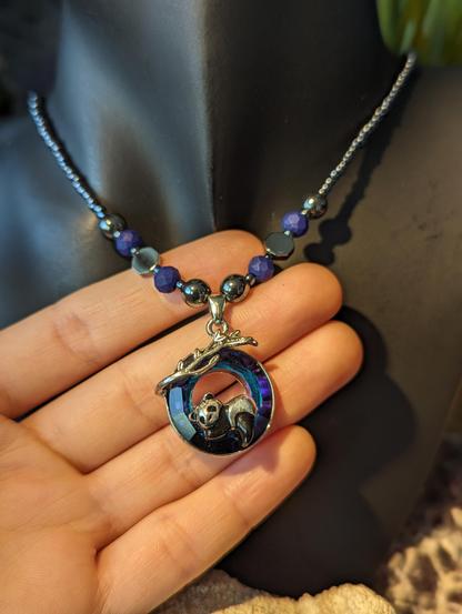 Handmade necklace with round glass blue pendant with a tiny metal panda lying in it and a silver leaf
Hematite styled beads and blue beads