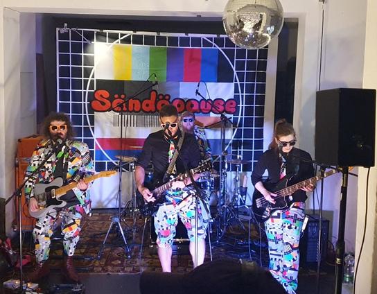 Band Sändäpause mit Banner wie ein altes TV Testbild und passenden bunten Anzügen