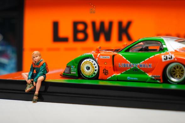 A girl with backpack sit beside Mazda RX-7 FD3S, LB-Super Silhouette Renown livery by iNNO64 in 1:64 scale with 1:64 figure on AREA 164
