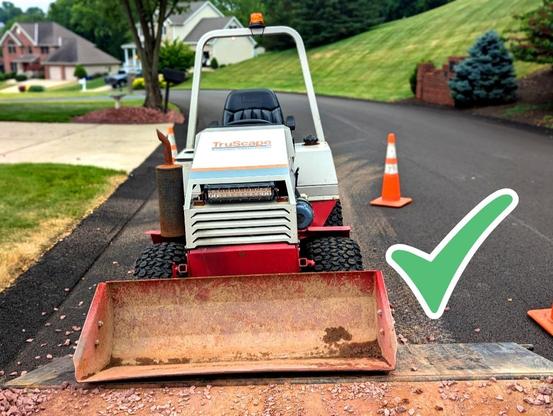 TruScape landscaping equipment parked on a residential street. The equipment is a compact utility machine with the TruScape logo visible on the front. The street is lined with orange traffic cones, and a well-maintained suburban neighborhood is visible in the background.