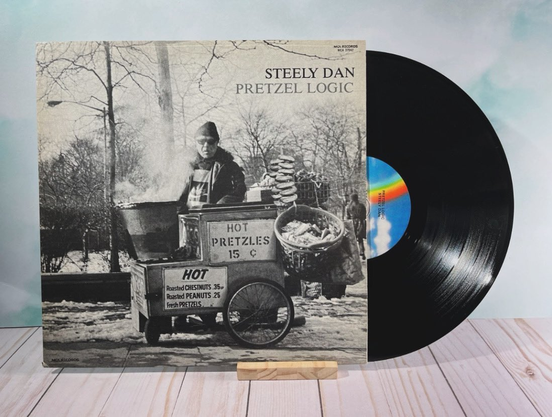 Photo of the Black & White cover of the Pretzel Logic album and its corresponding vinyl record halfway into the sleeve. 

The cover famously features the name of the band & album title in the top right. And the photo featured on the cover is a black and white of a pretzel vendor in NYC with steam coming out of his roasted chestnut barrel. 

Photo of record borrowed from this tweet:

https://x.com/MichaelLeonhart/status/1760738830657966561/photo/1