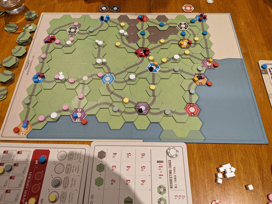 Age of Steam game in progress showing pastel circle pieces, and lots of hexagons containing railway track