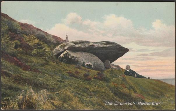 A vintage colour postcard showing a gentleman lying down beside the prehistoric burial chamber, the King's Quoit, overlooking Manorbier Bay on the coast of South West Wales, while a lady walks up the cliff beneath a pink and blue sky.