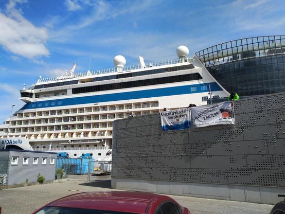 Menschen lassen zwei Protestbanner von der Landstromanlage in Kiel hängen. Im Hintergrund steht ein Kreuzfahrtschiff.