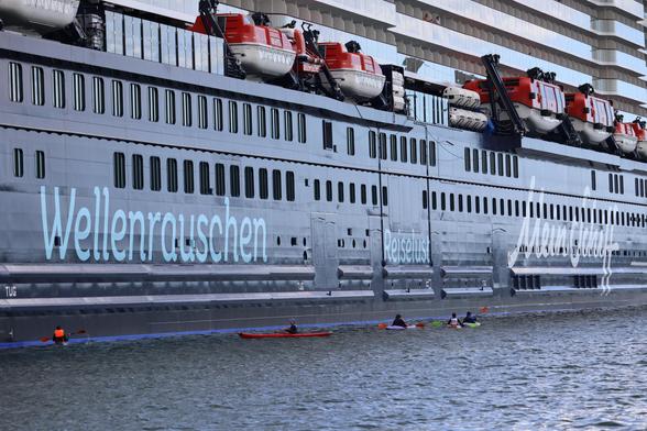 Menschen in Kajaks paddeln neben einem Kreuzfahrtschiff.