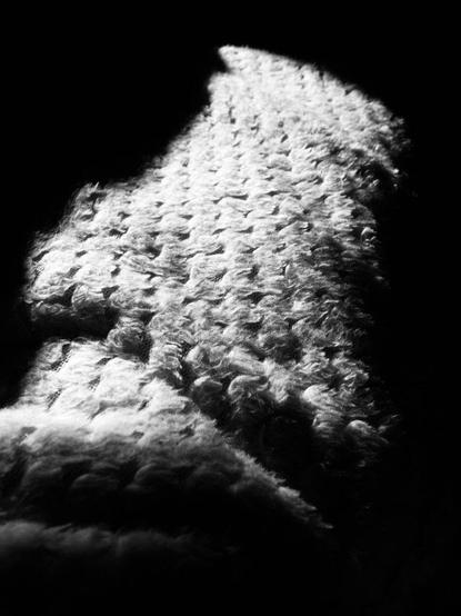 Monochrome shot of light on cross hatch patterned throw.surrounded by pure black the sun illuminates a high contrast overlap of patterned fabric