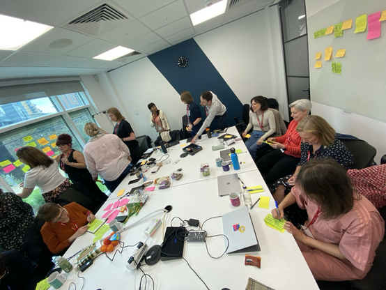 A room of people writing on sticky notes and adding those notes to glass windows.