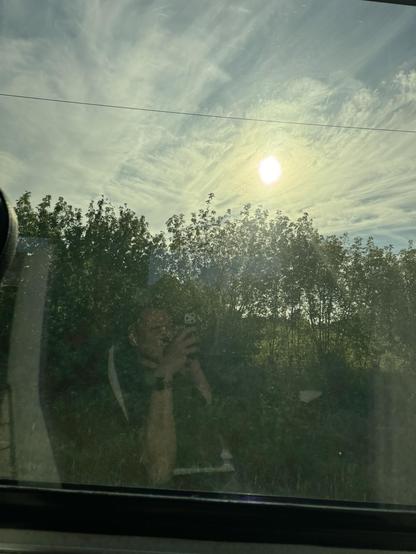 Me reflecting in a train window driving past trees and a slowly setting sun.