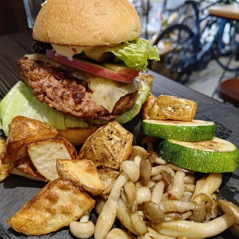 A hamburger with lettuce and sliced apple surrounded by potato wedges and fried mushrooms and zucchini, all on a black slate slab. 