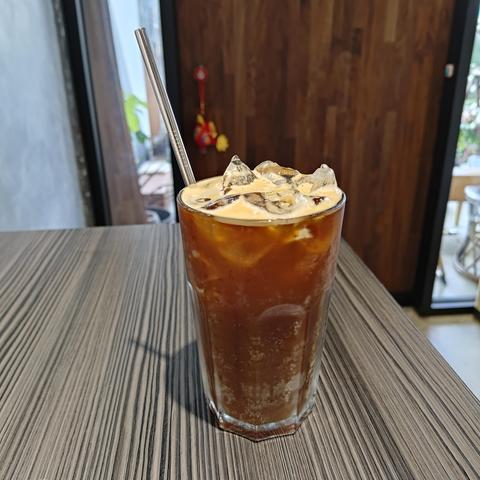 An iced coffee on a small table in a coffee shop. It has a metal straw.