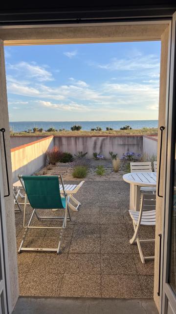Blick aus einer Terassentür auf eine kleine Terasse, dahinter erkennt mensch das Meer