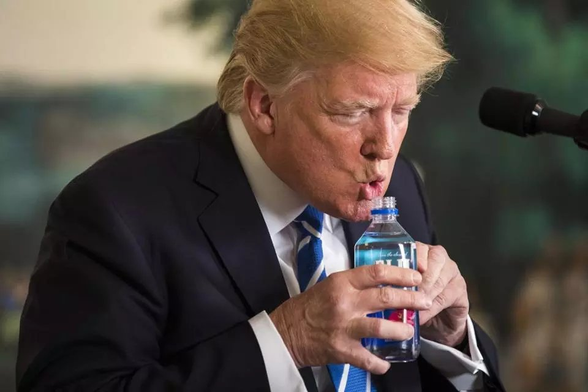 Donnie Trump (senior) holds a water bottle and is attempting to drink from it in a most peculiar way.  The water bottle is vertical in both hands and he has his lips pursed, as if he is about to blow out some candles.