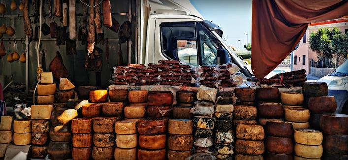 Ein riesiger Stapel verschiedenster sardischer Käsesorten, dazu regionale Wurstprodukte auf einem Wochenmarkt der Region. 