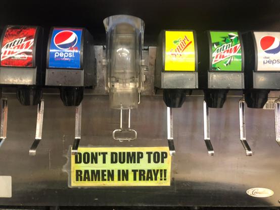A convenience store soda dispenser with a sign that reads “DON’T DUMP TOP RAMEN IN TRAY!!”