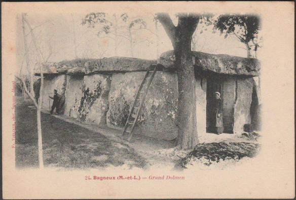 A vintage printed postcard of the prehistoric burial chamber the Grand Dolmen de Bagneux, measuring 17.3m x 5.4m x 3.1m and with a 4m antechamber, reputedly the largest dolmen in France, and in the whole world. A woman stands by the entrance and a gentleman stands at the side with a long stick. A ladder rests against the front side.