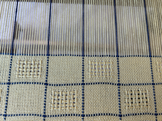 A close up look at alternating plain weave and lace blocks woven in yellow cotton on a hand loom