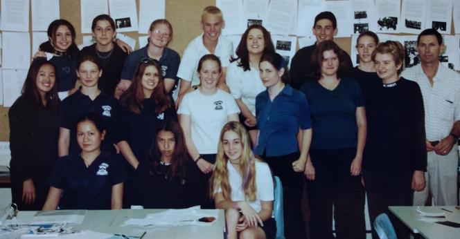 Colour; landscape orientation: A high school class (magazine committee) photo. Students are arranged in three rows and dressed in navy blue and white. Only two boys and fifteen girls! Teacher on the right, yours truly front-and-centre, which sounds much more celebratory than it was. I'm wearing my brother's old T-shirt. He probably threw a chair at me the day before.