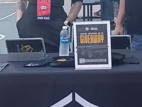 Image of a table with an AR-15 and a sign about the give away details 