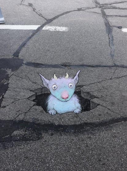 Zeichnung auf dem Boden.
David hat ein gezacktes Loch auf den Asphalt gemalt, aus welchem ein blau-violettes Schaf mit rosa Nase etwas betröppelt herausschaut.
