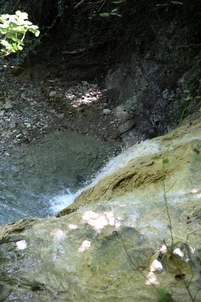 The image shows a serene scene of a small waterfall cascading over a rock ledge into a clear pool below