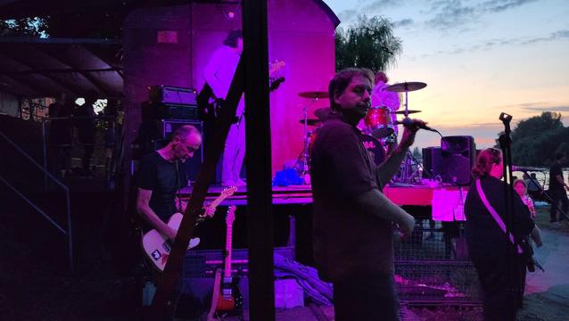 Es wird dunkel an der Außenbühne des Waggon... aber das kümmert doch House Williams (Fourpiece, Gesang, Schlagzeug, Bass, Gitarre) nicht, die in violett getauchtes Licht spielen. ;)

Edit: It's a five piece, actually. How could I miss a whole Guitar? 😉