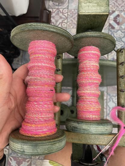 One full green bobbin and one partially full green bobbin. The yarn is neon pinks and yellows. 